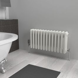 A 300mm x 605mm horizontal 3-column radiator in an White finish with chrome valves within a bathroom setting.
